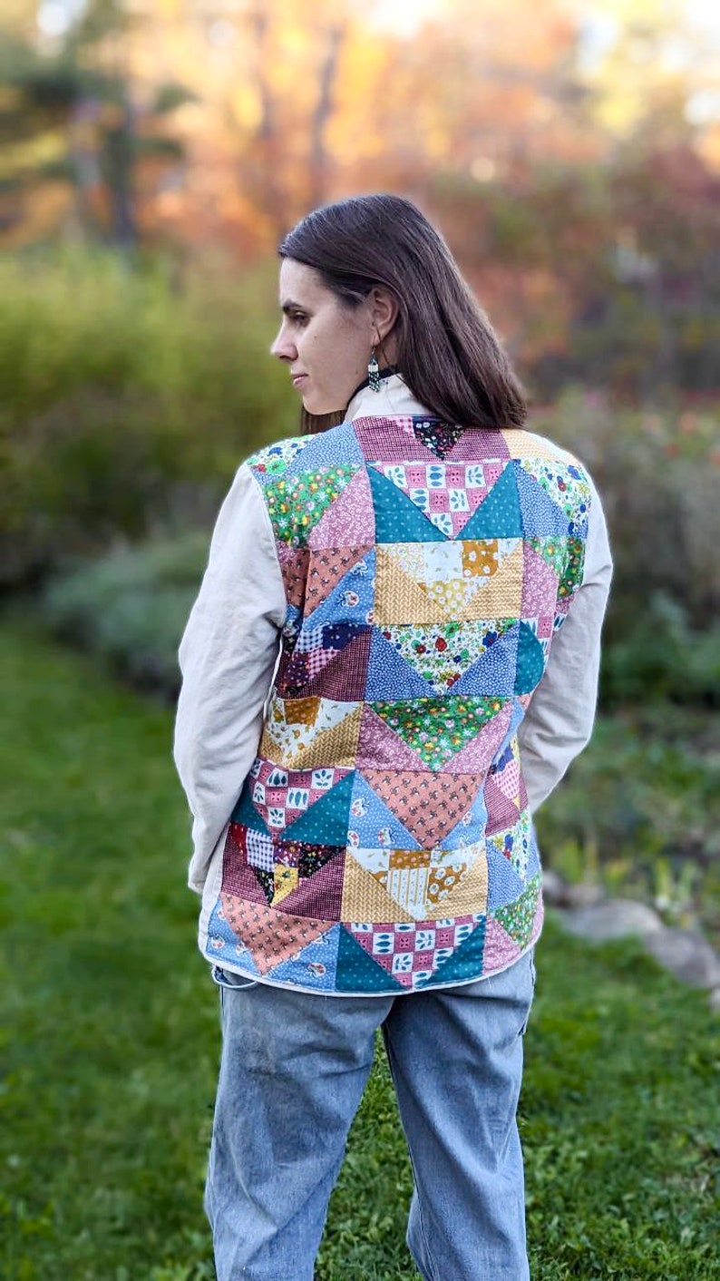May include: A woman wearing a white shirt with a patchwork quilt vest. The vest is made of various colorful fabrics with floral patterns. The woman is wearing blue jeans.