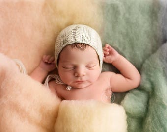 May include: A newborn baby wearing a white knitted hat sleeps peacefully on a multi-coloured fluffy blanket.
