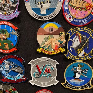 Może przedstawiać: Kolekcja haftowanych naszywek z r&oacute;żnymi motywami wojskowymi i lotniczymi. Naszywki są kolorowe i przedstawiają r&oacute;żne wzory, w tym samoloty, helikoptery, czaszki i zwierzęta. Niekt&oacute;re naszywki zawierają tekst, taki jak "Iron Horse", "VFA One Two Biz", "EAF", "MALS-13", "HMH-461", "HMH-368", "Strike Det", "NTP 19A", "Iceberg's Fulli", "Test Pilot School 178/19A", "'Murician", "Black Widows", "Co-West Boro", "HMLA-3528" i "German Flight Evaluation 2021".