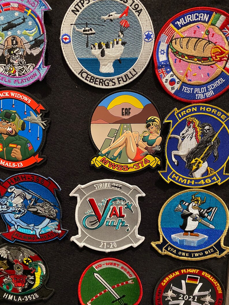 Może przedstawiać: Kolekcja haftowanych naszywek z r&oacute;żnymi motywami wojskowymi i lotniczymi. Naszywki są kolorowe i przedstawiają r&oacute;żne wzory, w tym samoloty, helikoptery, czaszki i zwierzęta. Niekt&oacute;re naszywki zawierają tekst, taki jak "Iron Horse", "VFA One Two Biz", "EAF", "MALS-13", "HMH-461", "HMH-368", "Strike Det", "NTP 19A", "Iceberg's Fulli", "Test Pilot School 178/19A", "'Murician", "Black Widows", "Co-West Boro", "HMLA-3528" i "German Flight Evaluation 2021".