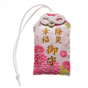 Puede incluir: Una bolsa de tela blanca con un estampado floral rosa y caracteres japoneses dorados que dicen "幸福神守" (Felicidad, Dios, Protecci&oacute;n). La bolsa tiene un cord&oacute;n blanco.