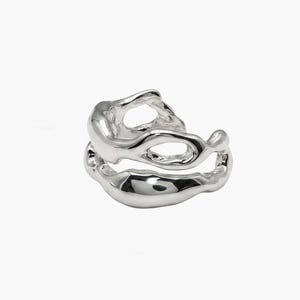 Pu&ograve; includere: Un anello d'argento dal design organico e fluido. L'anello presenta due fasce collegate con forme irregolari e fluide, creando un'estetica astratta e moderna. Il metallo lucido riflette la luce.