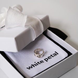 Pu&ograve; includere: Un orecchino a polsino argentato dal design organico &egrave; presentato in una confezione regalo bianca legata con un nastro bianco. La scatola contiene un panno bianco con la scritta "white petal".