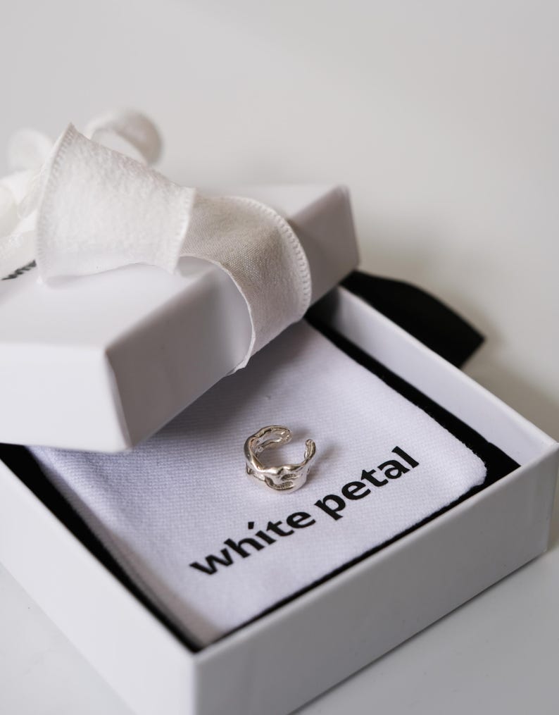 Pu&ograve; includere: Un orecchino a polsino argentato dal design organico &egrave; presentato in una confezione regalo bianca legata con un nastro bianco. La scatola contiene un panno bianco con la scritta "white petal".
