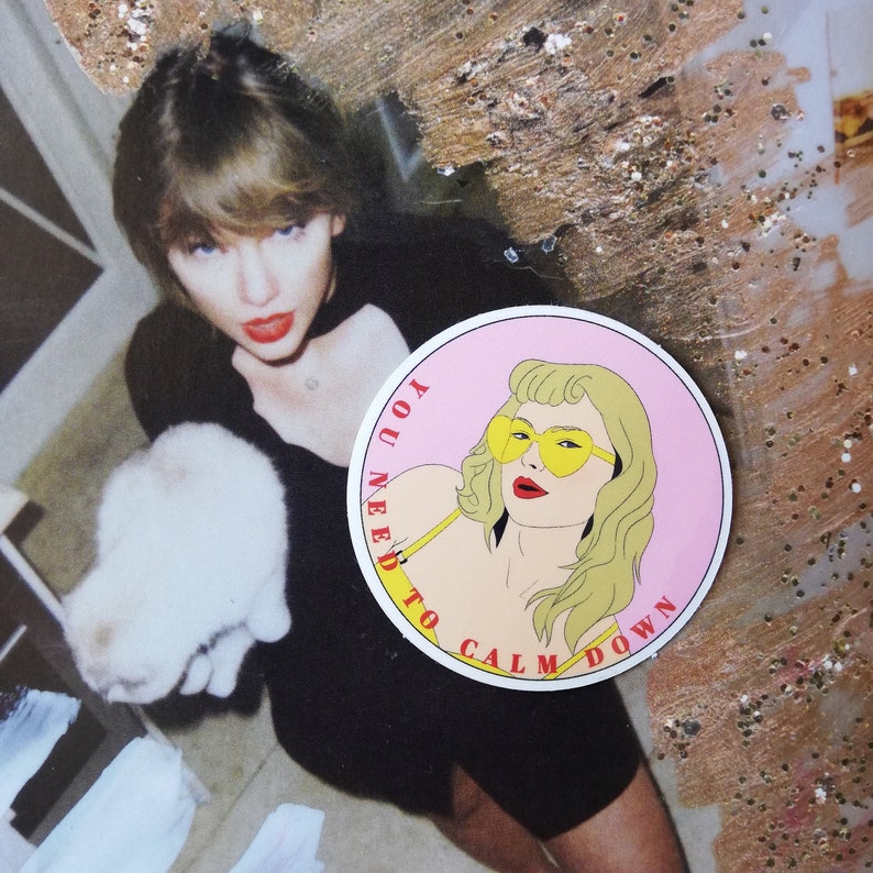 May include: A pink and white round sticker with a cartoon illustration of a woman wearing yellow sunglasses and a yellow top. The text on the sticker reads "You need to calm down".