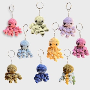 Könnte beinhalten: Zehn gehäkelte Octopus-Schlüsselanhänger in verschiedenen Farben, darunter rosa, blau, gelb und grün. Jeder Octopus hat acht Tentakel und ist an einem silbernen Schlüsselring befestigt.