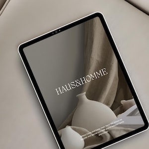 May include: A tablet screen displaying a minimalist design with the text "HAUS&HOMME" and a white ceramic vase on a brown fabric background. The text below the logo reads "Where house and home meet, there can always be laughter and special moments shared between family and friends."