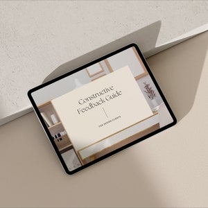 Puede incluir: Una tableta mostrando una guía digital titulada "Constructive Feedback Guide for Design Clients". La guía se muestra sobre un fondo blanco con un estante de madera marrón claro y un jarrón de flores en el fondo.