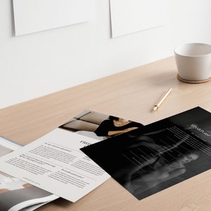 May include: A black and white photo of a woman sitting on a couch. The photo is part of a brochure with the text "Mission and Values" printed on it. The brochure is on a wooden table with a white coffee mug and a pen.