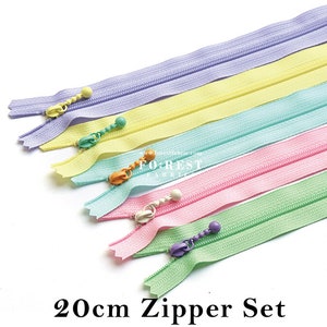 Könnte beinhalten: Satz mit fünf 20 cm langen Reißverschlüssen in Pastellfarben: Lavendel, Gelb, Hellblau, Rosa und Grün. Jeder Reißverschluss hat einen Kunststoff-Schieber mit einer kleinen Perle.