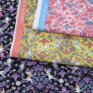 May include: Three fabric swatches with whimsical patterns featuring cats, flowers, and other whimsical designs. The fabrics are in shades of pink, yellow, and black. The text "JOUE FLEUR LA TOILE" is visible on the pink fabric.