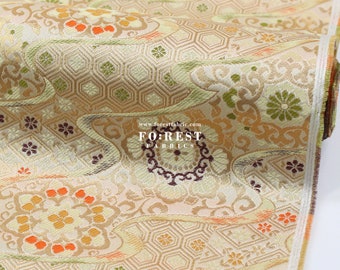 Puede incluir: Primer plano de una tela dorada y crema con un patrón repetitivo de flores, espirales y formas geométricas. La tela tiene un brillo sutil y una superficie texturizada. El texto "FOREST FABRICS" y "www.forestfabric.com" es visible en el centro inferior de la imagen.