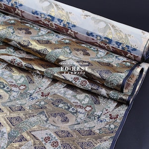 May include: Close-up of a fabric with a gold, green, and blue pattern. The fabric has a traditional Japanese design with flowers, birds, and geometric shapes. The fabric is folded and layered, showing the intricate details of the pattern.
