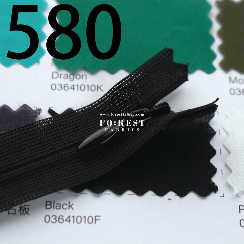 May include: Close-up of a black zipper with a black pull tab. The number "580" is printed in large black font above the zipper. The text "Dragon" and "Black" are printed on white tags. The website "www.forestfabric.com" is visible.