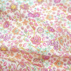 Op de afbeelding: Witte stof met een herhalend patroon van roze, paarse en groene bloemen met gouden accenten. De bloemen zijn versierd met kleine, glinsterende juwelen.