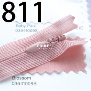 May include: A close-up of a baby pink zipper with a matching fabric swatch. The zipper is open, revealing the teeth and slider. The fabric swatch is a lighter shade of pink. The number "811" is printed in black at the top of the image.