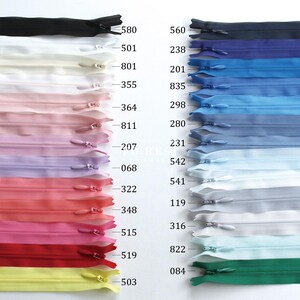 May include: A collection of colorful nylon zippers in various shades, including black, white, pink, blue, and green. Each zipper is closed and features a metal slider. The image showcases a range of colors and zipper sizes, suitable for sewing and crafting projects.