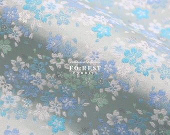 May include: Close-up of a fabric with a floral pattern. The fabric features a repeating design of blue, light blue, and white flowers on a pale green background. The text "FOREST FABRICS" is visible. The fabric appears to be soft and flowing.