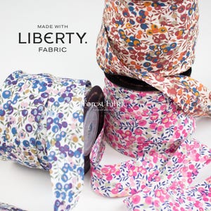 Può includere: Bobine di nastro in tessuto Liberty con vari motivi floreali. I nastri presentano un mix di colori, tra cui blu, rosa, arancione e bianco. Il testo "MADE WITH LIBERTY. FABRIC" è visibile. Il sito web "forestfabric.com" è anch'esso visibile.