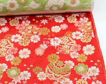 May include: Red fabric with a repeating pattern of gold and green stylized balls, white and pink flowers, and gold stars. The fabric is folded over, revealing a green and white floral pattern on the underside. The text "www.forestfabrics.com" and "FOREST FABRICS" is visible on the fabric.