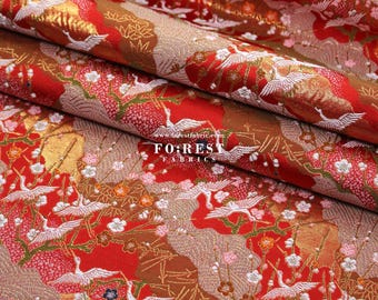 Pode incluir: Tecido vermelho com um padrão de guindaste dourado e branco. O tecido tem um aspecto texturizado, tecido e é perfeito para projetos de artesanato ou costura.