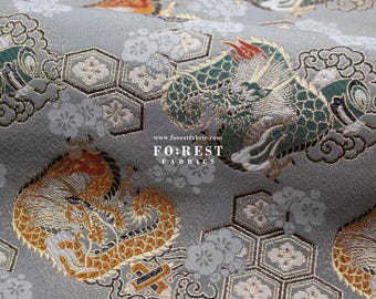 Puede incluir: Tela gris con un patrón repetido de dragones verdes y dorados, formas hexagonales y flores estilizadas. La tela tiene el texto "FOREST FABRICS" y "www.forestfabric.com" impreso en ella.