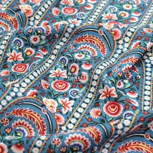 May include: Close-up of a blue fabric with a floral paisley pattern. The design features red, white, and yellow flowers and leaves. The fabric has a repeating pattern with vertical stripes and the text "FO:REST FABRIC".
