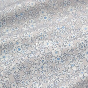 May include: A close-up of a light gray fabric with a white and blue floral pattern. The fabric is soft and has a subtle sheen. The pattern is small and delicate, and it is repeated throughout the fabric. The fabric is perfect for quilting, sewing, and crafting.