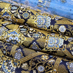 May include: Close-up of a black fabric with a gold and blue floral pattern. The fabric is woven with a raised texture and has a luxurious feel. The fabric is folded in a way that shows the intricate details of the design.