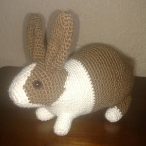 May include: A brown and white crocheted rabbit toy with a brown nose and black eyes.