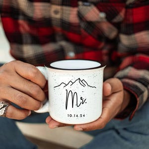 May include: White ceramic mug with a black rim and handle. The mug has a black and white mountain range design with the word "Mr." and the date "10.14.24" printed on it.
