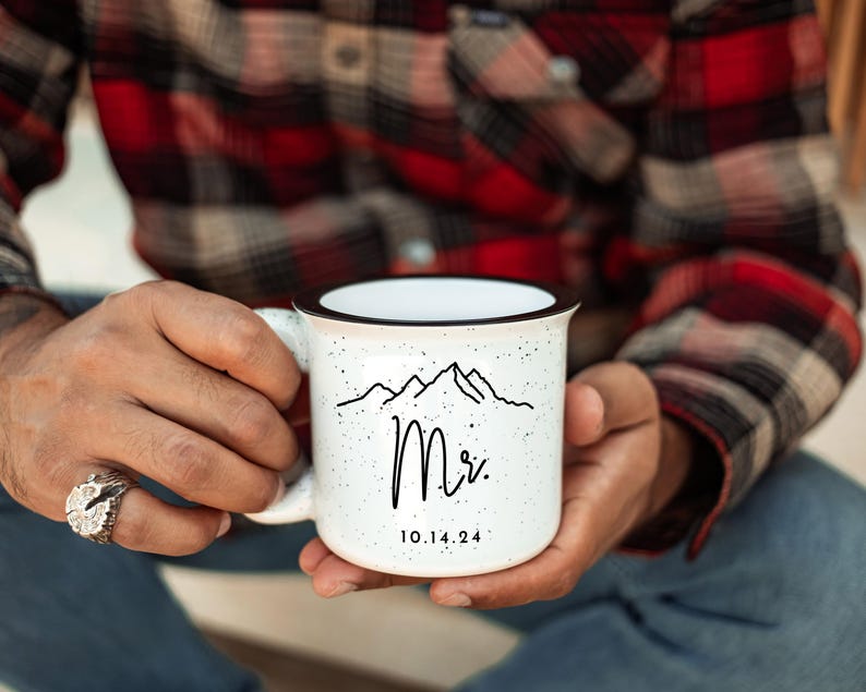 May include: White ceramic mug with a black rim and handle. The mug has a black and white mountain range design with the word "Mr." and the date "10.14.24" printed on it.