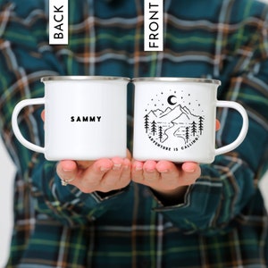 May include: Two white enamel camping mugs. One mug has the text "SAMMY" on the front. The other mug has a black and white illustration of mountains, a river, trees, and a crescent moon with stars. The text "ADVENTURE IS CALLING" is below the illustration.