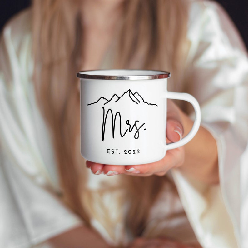 May include: White enamel mug with a black mountain range design and the text "Mrs. EST. 2022".