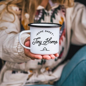 May include: White enamel mug with a black rim and handle. The mug has the text "Home Sweet Tiny Home" with a small house icon underneath.