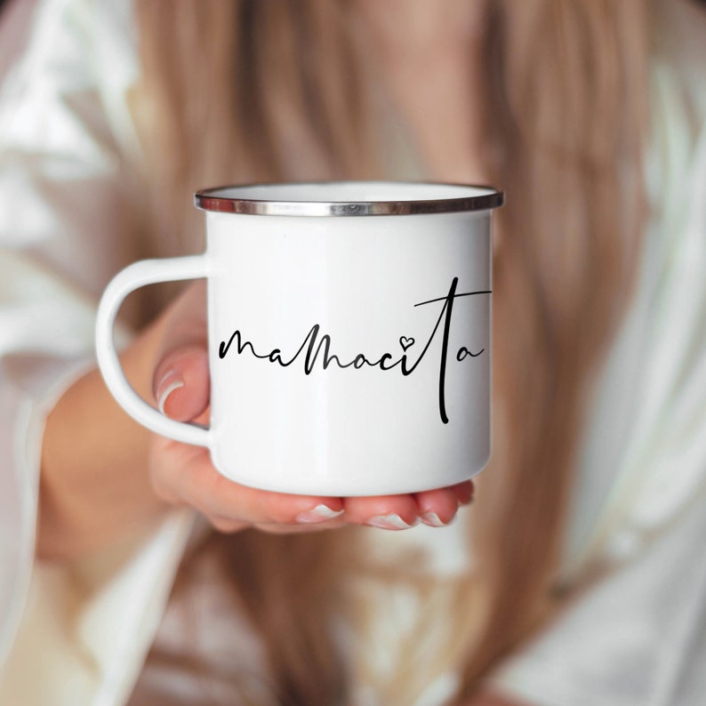 Puede incluir: Taza de esmalte blanco con borde plateado y texto en cursiva negra que dice "mamacita" con un peque&ntilde;o s&iacute;mbolo de coraz&oacute;n.