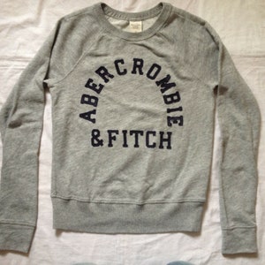 May include: Grey long-sleeved sweatshirt with a navy blue embroidered logo that reads "Abercrombie & Fitch".