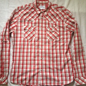 May include: A red and white checked long-sleeved button-down shirt with a pointed collar and two chest pockets. The shirt has a Western-style design with pearl-like buttons.