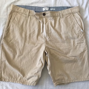 May include: A pair of beige cargo shorts with a blue and white striped waistband. The shorts have a brand label that says "Quiksilver" and "Straight Fit".