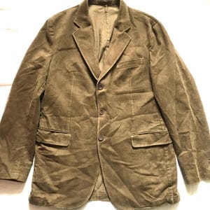 May include: A brown corduroy blazer with a classic three-button closure, two front pockets, and a notched lapel. The jacket has a tailored fit and a soft, textured appearance, suitable for casual or semi-formal wear.