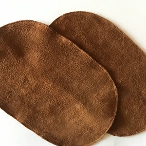 Peut inclure: Deux patchs en cuir suédé marron, de forme ovale, avec une texture lisse.