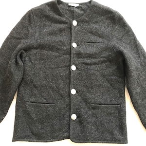 Puede incluir: Chaqueta gris oscuro con cuello redondo y cuatro botones blancos. Tiene dos bolsillos delanteros y un pequeño bolsillo en el pecho. La tela parece una suave mezcla de lana. Diseño clásico.
