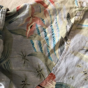 May include: A light blue shirt with a floral pattern. The pattern features pink, blue, and green flowers and leaves. The shirt has a button-up collar and a long sleeve.