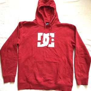 May include: A white ceramic mug with a black handle and the text "But First, Coffee" in a bold, black font. The mug is set against a blurred background, suggesting a cozy setting.