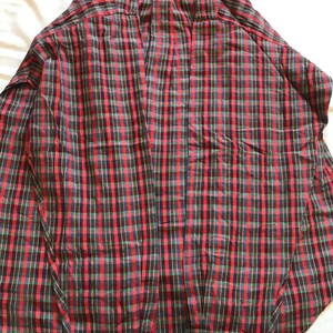 Puede incluir: Una camisa a cuadros roja, negra y verde con botones. La camisa de manga larga tiene pu&ntilde;os abotonados y un cuello cl&aacute;sico. El dise&ntilde;o a cuadros es una cuadr&iacute;cula repetida de l&iacute;neas rojas, negras y verdes.