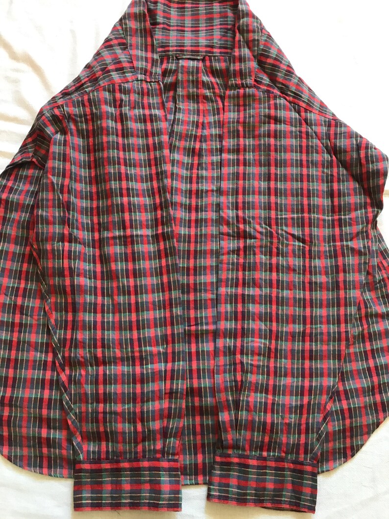 Puede incluir: Una camisa a cuadros roja, negra y verde con botones. La camisa de manga larga tiene pu&ntilde;os abotonados y un cuello cl&aacute;sico. El dise&ntilde;o a cuadros es una cuadr&iacute;cula repetida de l&iacute;neas rojas, negras y verdes.