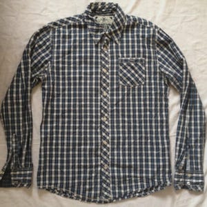 May include: A long-sleeved button-down shirt in a blue and white checkered pattern. The shirt has a single pocket on the chest and a button-down collar. The cuffs are buttoned, and the shirt is made of a lightweight fabric.