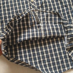May include: A blue and white plaid button-down shirt. The shirt has a classic collar and buttoned cuffs. The fabric is a woven cotton with a small tag that reads "THANK YOU".
