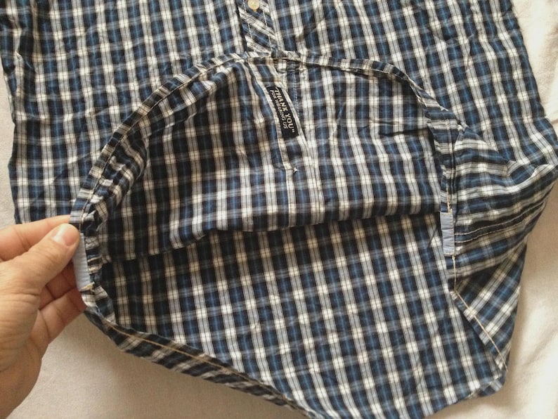 May include: A blue and white plaid button-down shirt. The shirt has a classic collar and buttoned cuffs. The fabric is a woven cotton with a small tag that reads "THANK YOU".