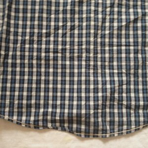 May include: Close-up of a blue, white, and black plaid shirt. The fabric is a woven pattern of small squares. The shirt has long sleeves and a curved hemline. The shirt is made of a soft, comfortable material.